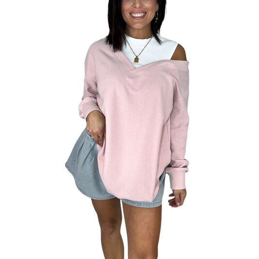 Woman wearing a pink off-shoulder sweater over a white shirt with denim shorts on a white background