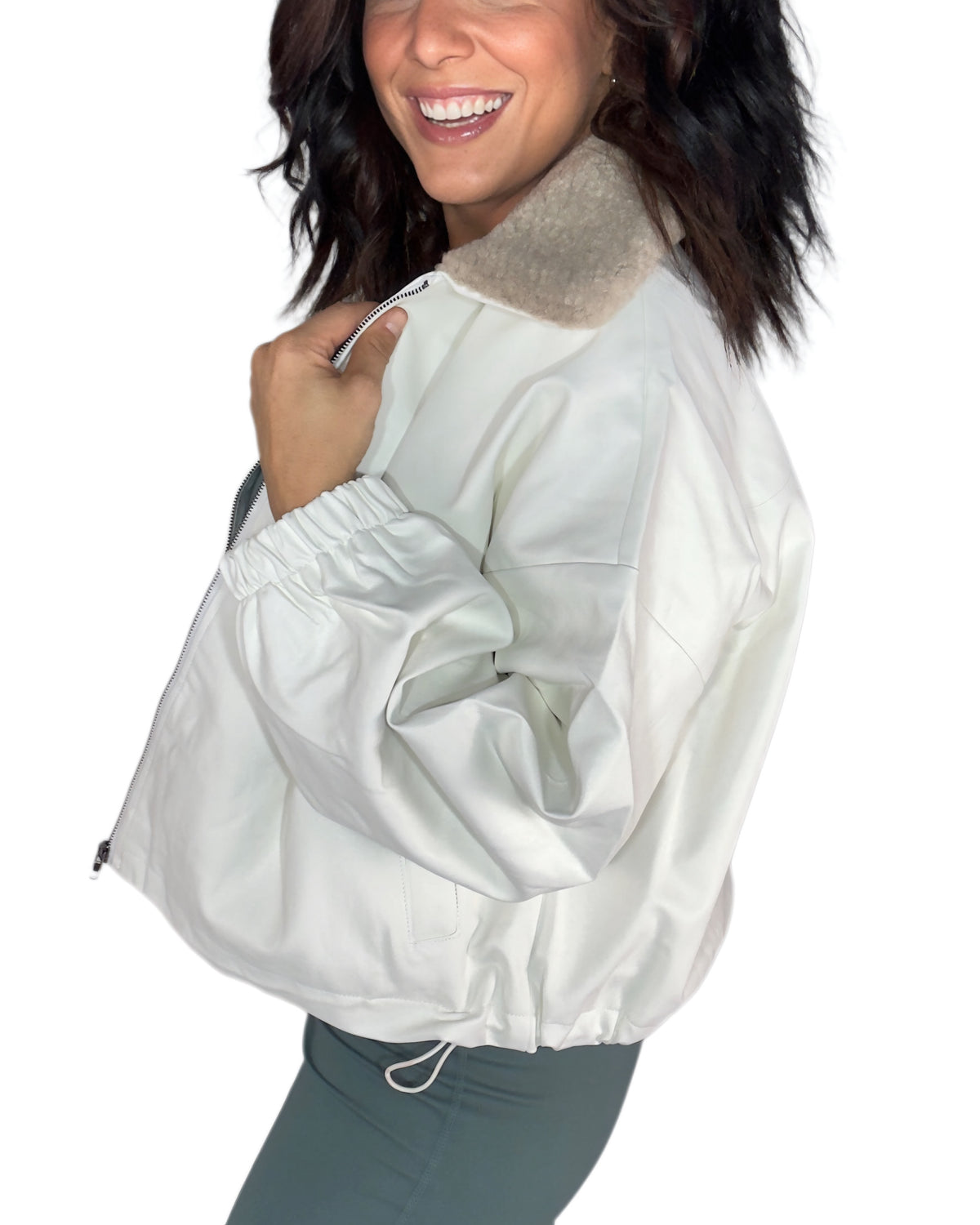 Side profile of a woman wearing an off white jacket with tan sherpa around the collar with green active pants, on a white background 