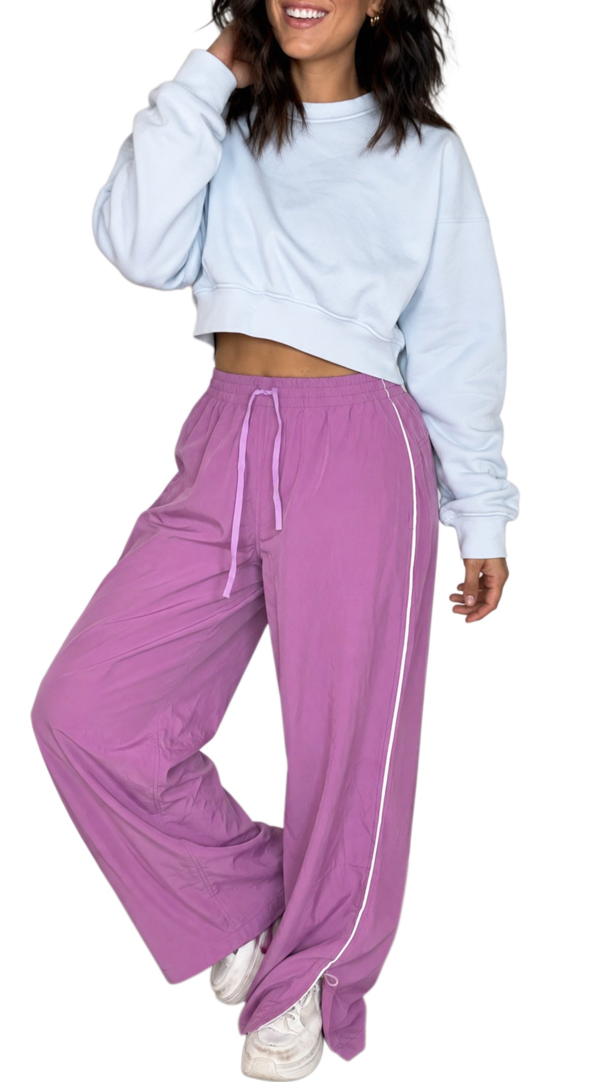 Woman wearing mulberry color track pants with a drawstring and white line going down the side with a light blue cropped sweatshirt on a white background