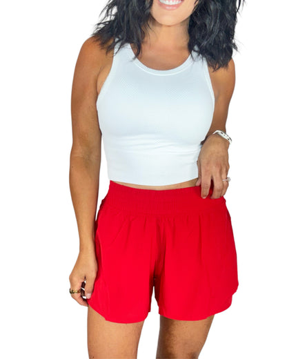Woman wearing a white crop top and red shorts on a white background