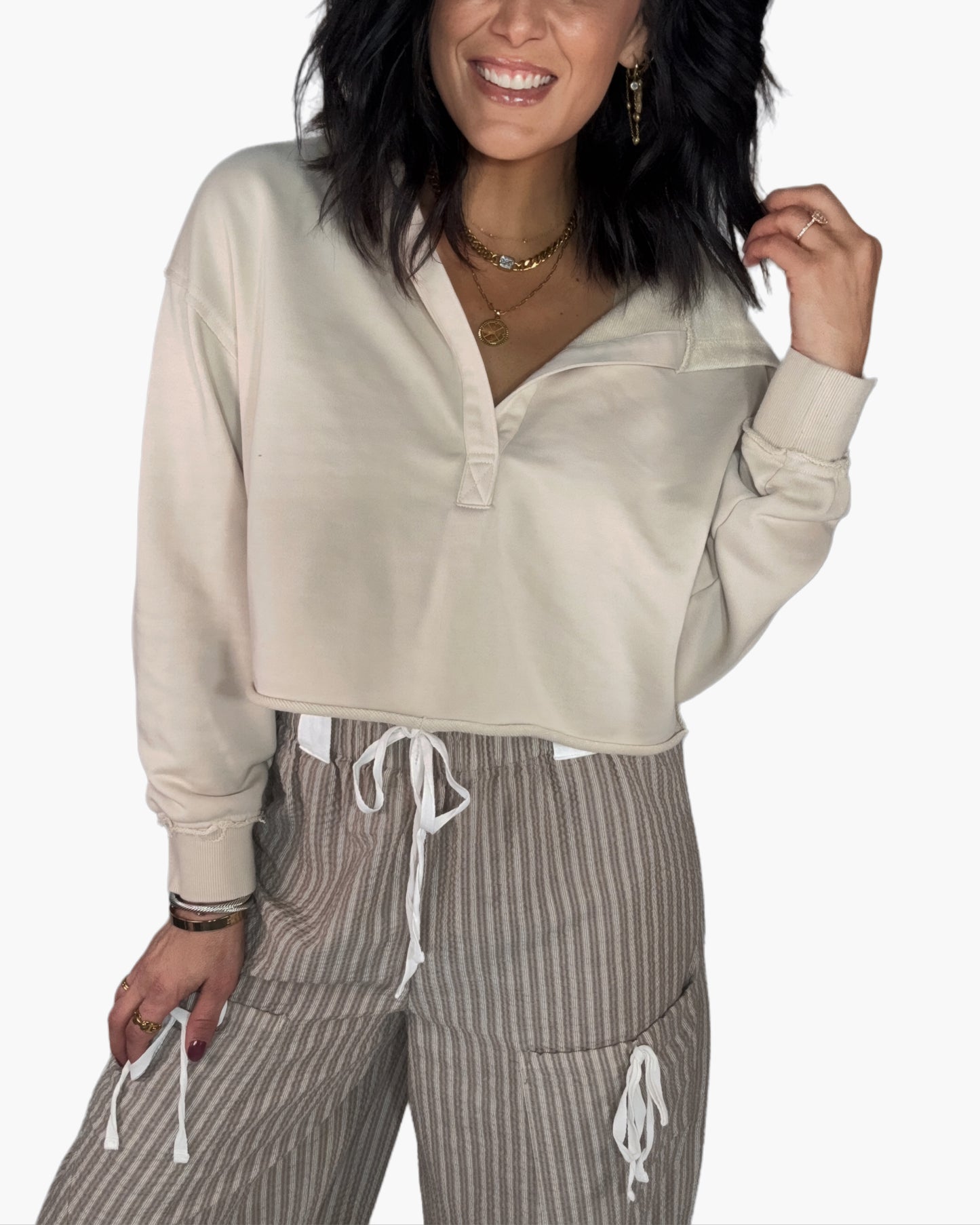 Close up of a woman wearing a beige cropped hoodie and striped pants on a white background