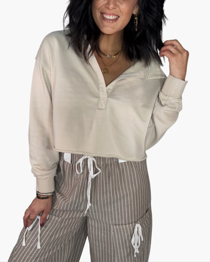 Close up of a woman wearing a beige cropped hoodie and striped pants on a white background
