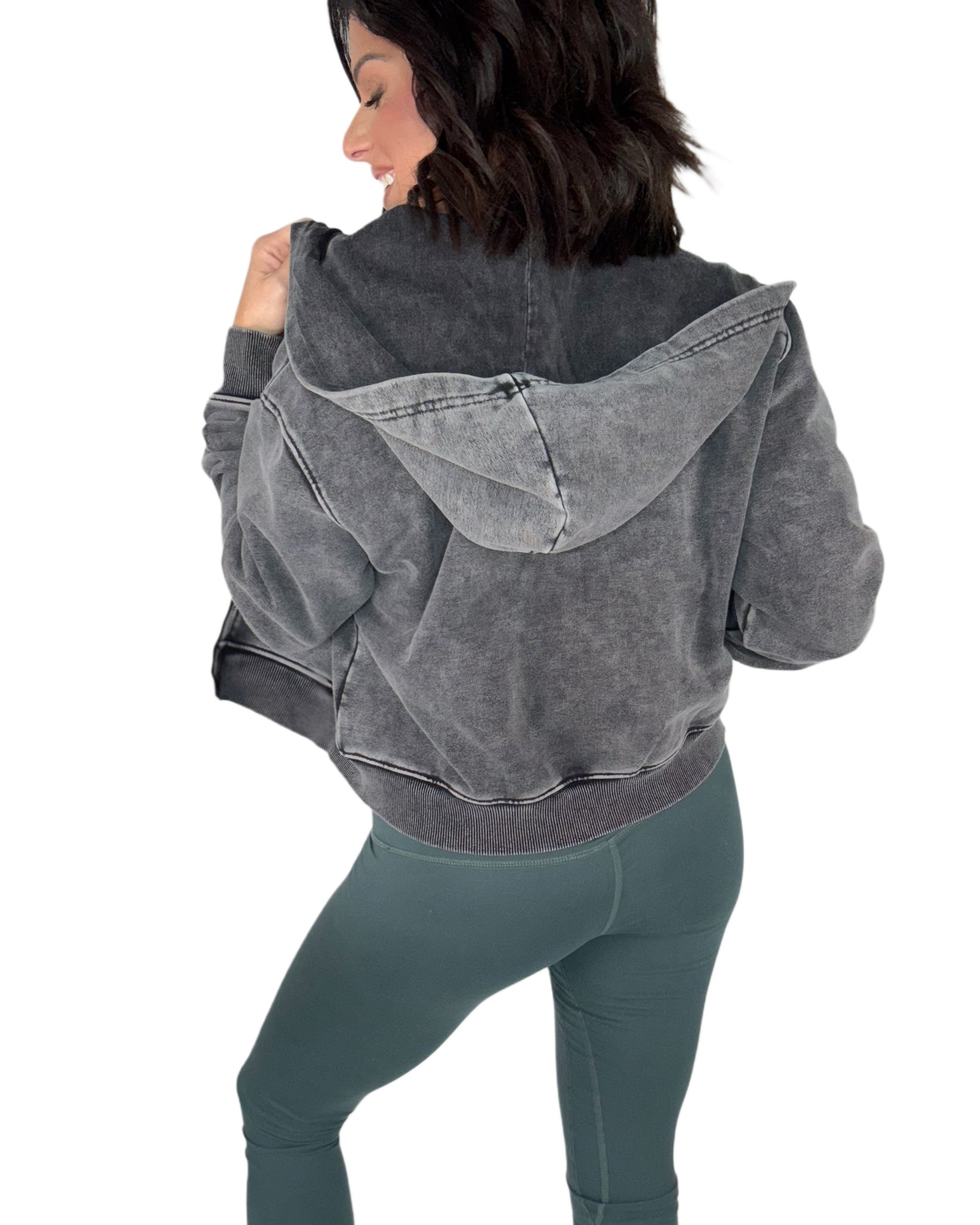 Woman turned around wearing a gray acid washed hoodie and green leggings on a white background