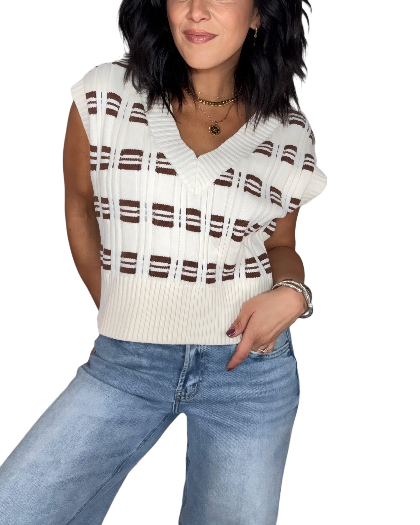 Woman wearing a white and brown striped sweater vest with blue jeans on a white background