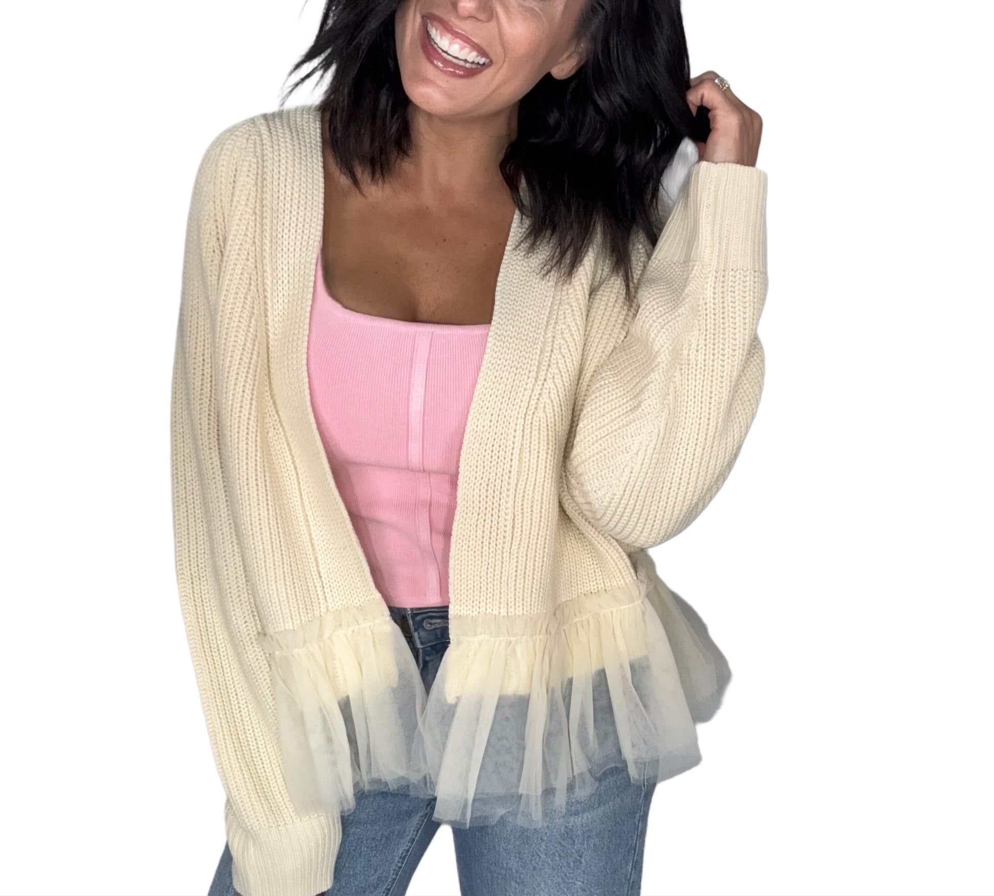 Woman wearing a cream cardigan with tulle at the bottom over a pink top and jeans on a white background