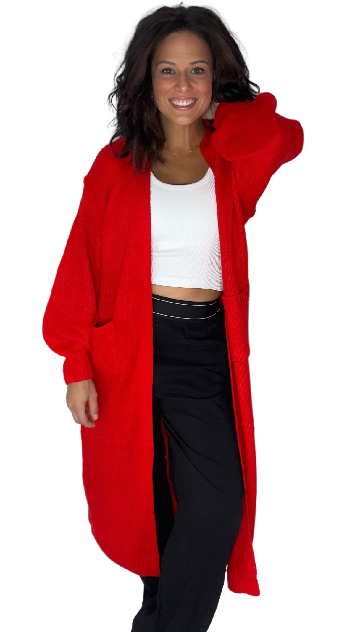 A woman modeling a bright red open-front cardigan or long coat over a white crop top and black pants, photographed against a plain white studio background.