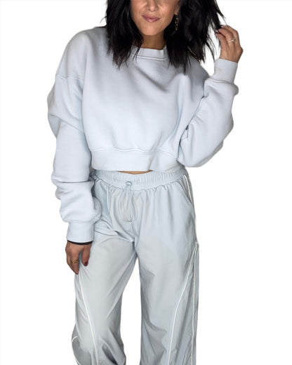 Woman wearing a light blue cropped sweatshirt with matching track pants, on a white background 