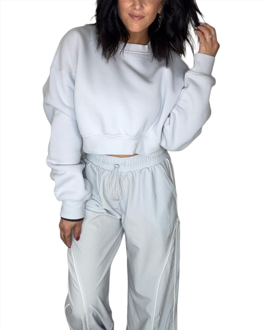 Woman wearing a light blue cropped sweatshirt with matching track pants, on a white background 