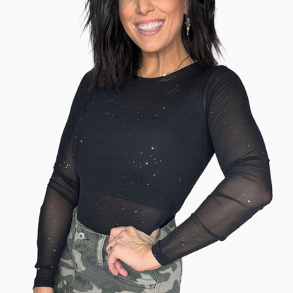 Side profile of a woman wearing a black long-sleeve mesh top with silver specks on it on a white background