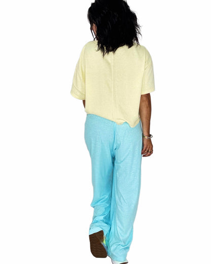 Back profile of a woman wearing bright blue sweats with a yellow tee on a white background