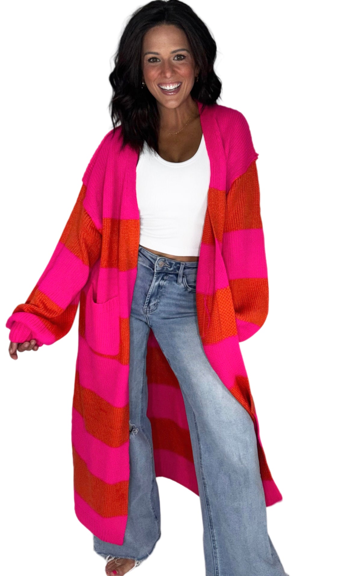 Woman smiling wearing a stripped pink and red cardigan with jeans on a white background 