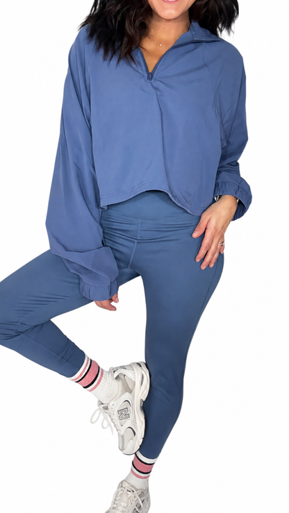 Woman wearing blue active leggings with a matching half zip on a white background