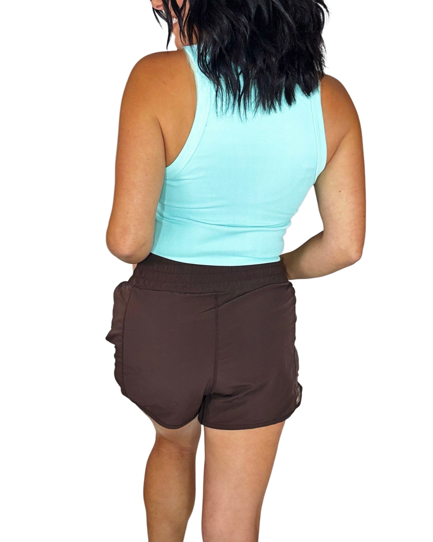 Back profile of a woman wearing brown active shorts with a blue ribbed tank on a white background