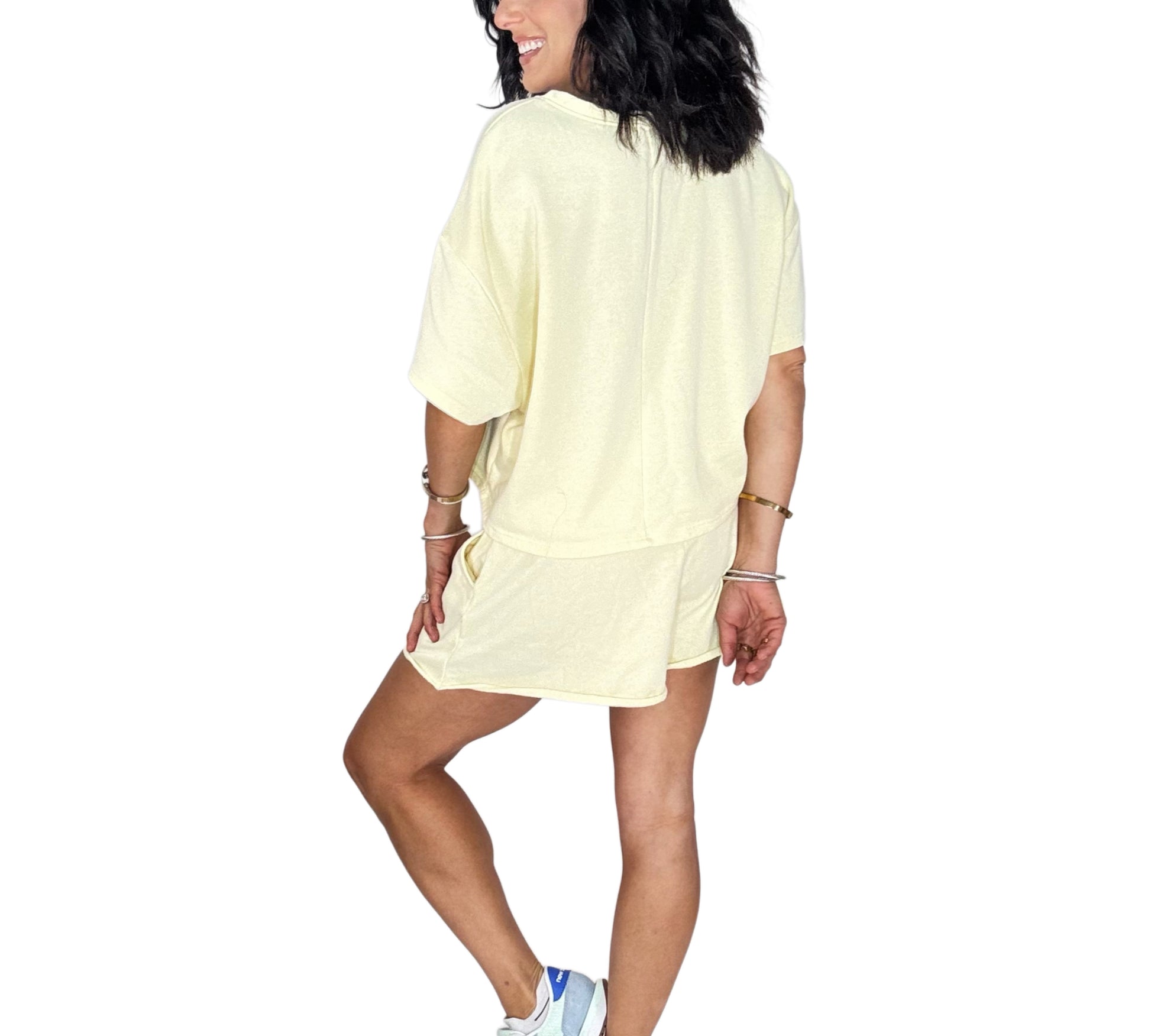 Back profile of a woman wearing a pale yellow short set on a white background
