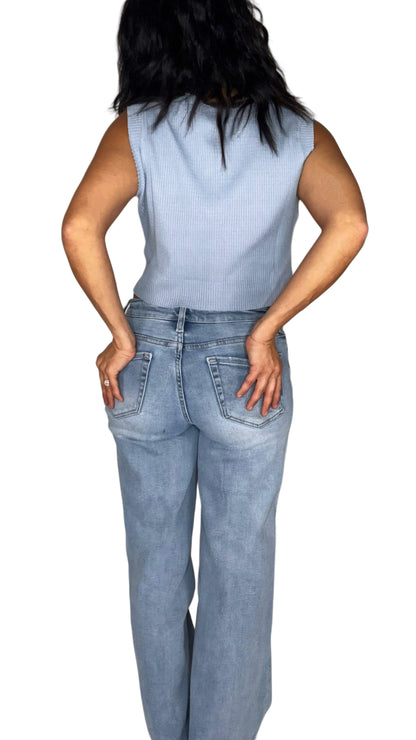 Back profile of a woman wearing  a light blue waffle sleeveless top with medium wash jeans, on a white background