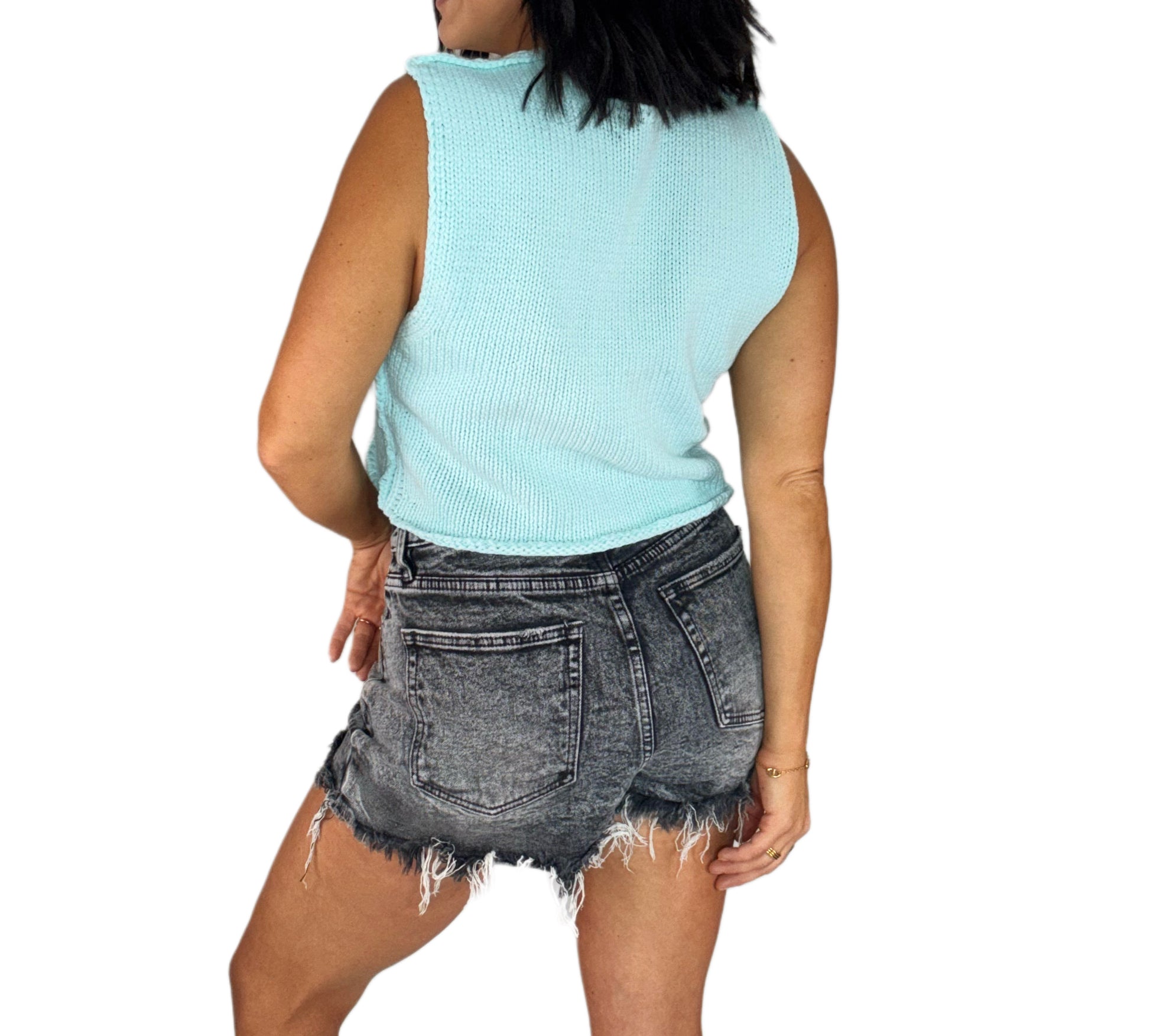 Back profile of a woman wearing a light blue sleeveless top and black denim shorts on a white background