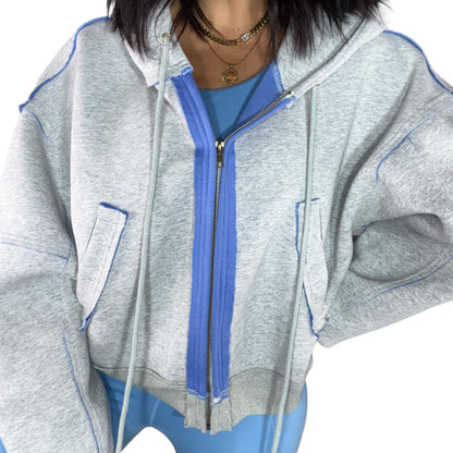 Close up of a woman wearing a gray hoodie with blue accents and matching leggings on a white background