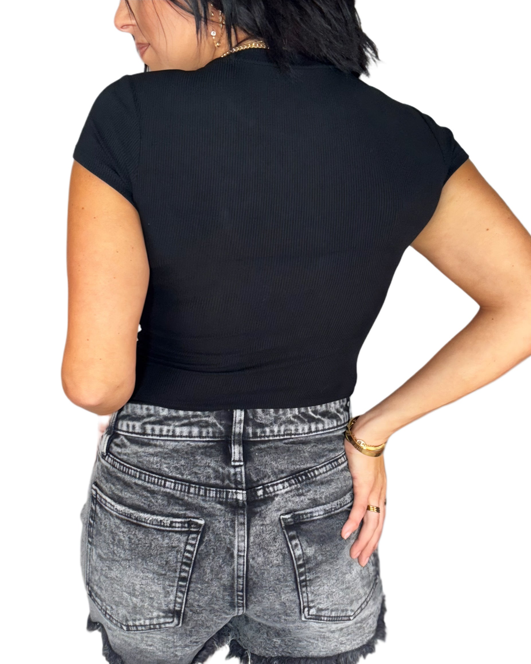 Woman turned around wearing a black ribbed bodysuit and gray denim shorts on a white background