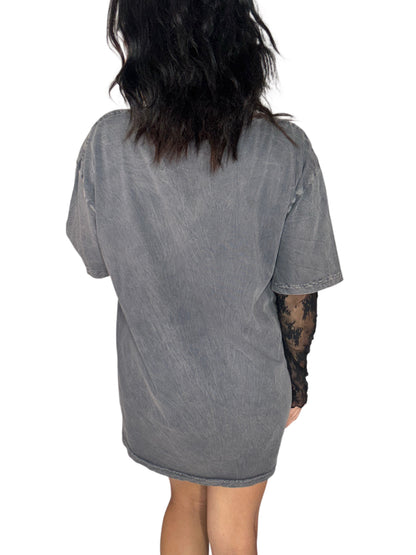 Back profile of a woman wearing a deep grey Halloween skeleton tee that says "staying alive" with a lace undershirt on white background 