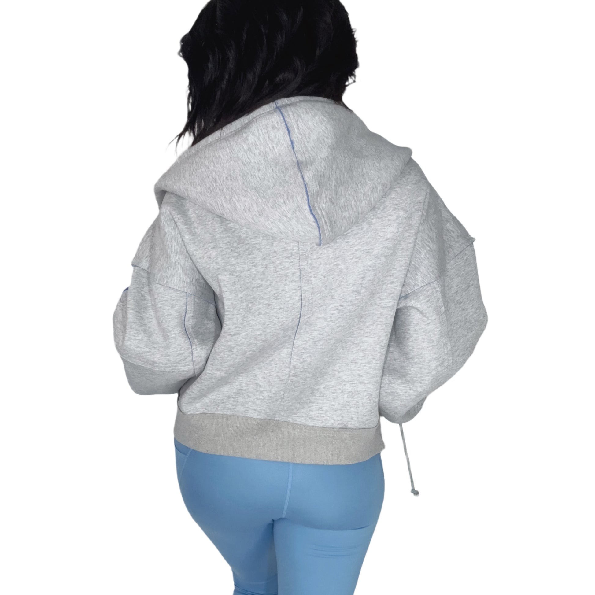 Back profile of a woman wearing a gray hoodie with blue accents and matching leggings on a white background