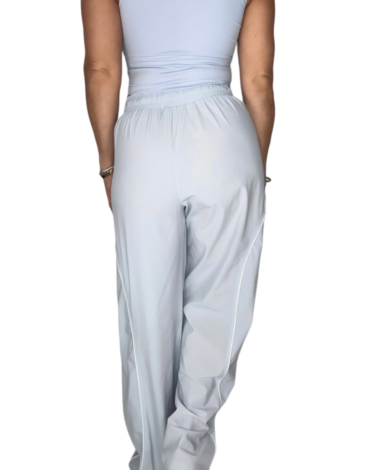 Back profile of a woman wearing light blue track pants with matching tank, on a white background