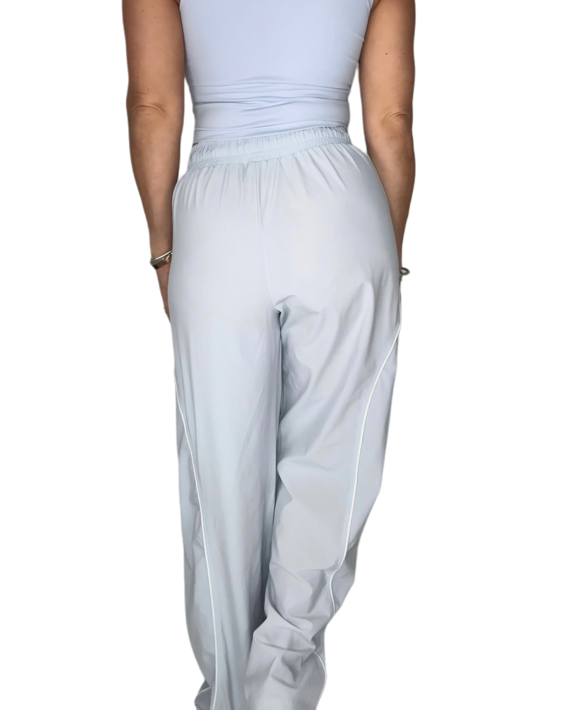 Back profile of a woman wearing light blue track pants with matching tank, on a white background