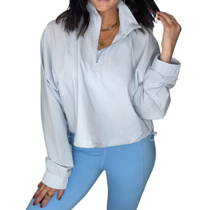 Woman wearing a light blue windbreaker pullover with powder blue leggings and a white background