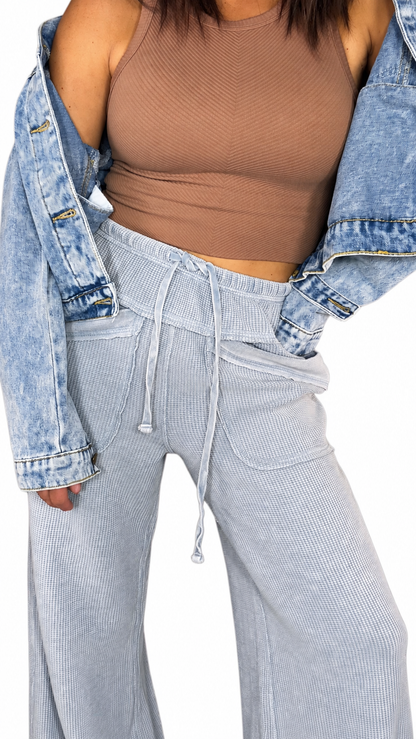 Close up of a woman wearing waffle light blue casual pants with a drawl string and front pockets with a brown tank and jean jacket on a white background