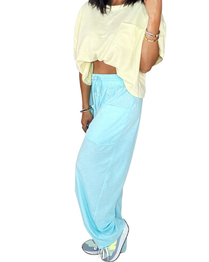 Close up of a woman wearing bright blue sweat pants, with a yellow tee, on a white background