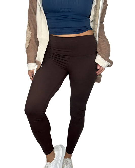 Woman wearing brown leggings, blue top, and creamed brown  jacket on a white background