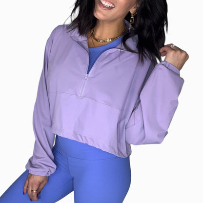 Side profile of a woman wearing a purple half-zip jacket and blue leggings on a white background