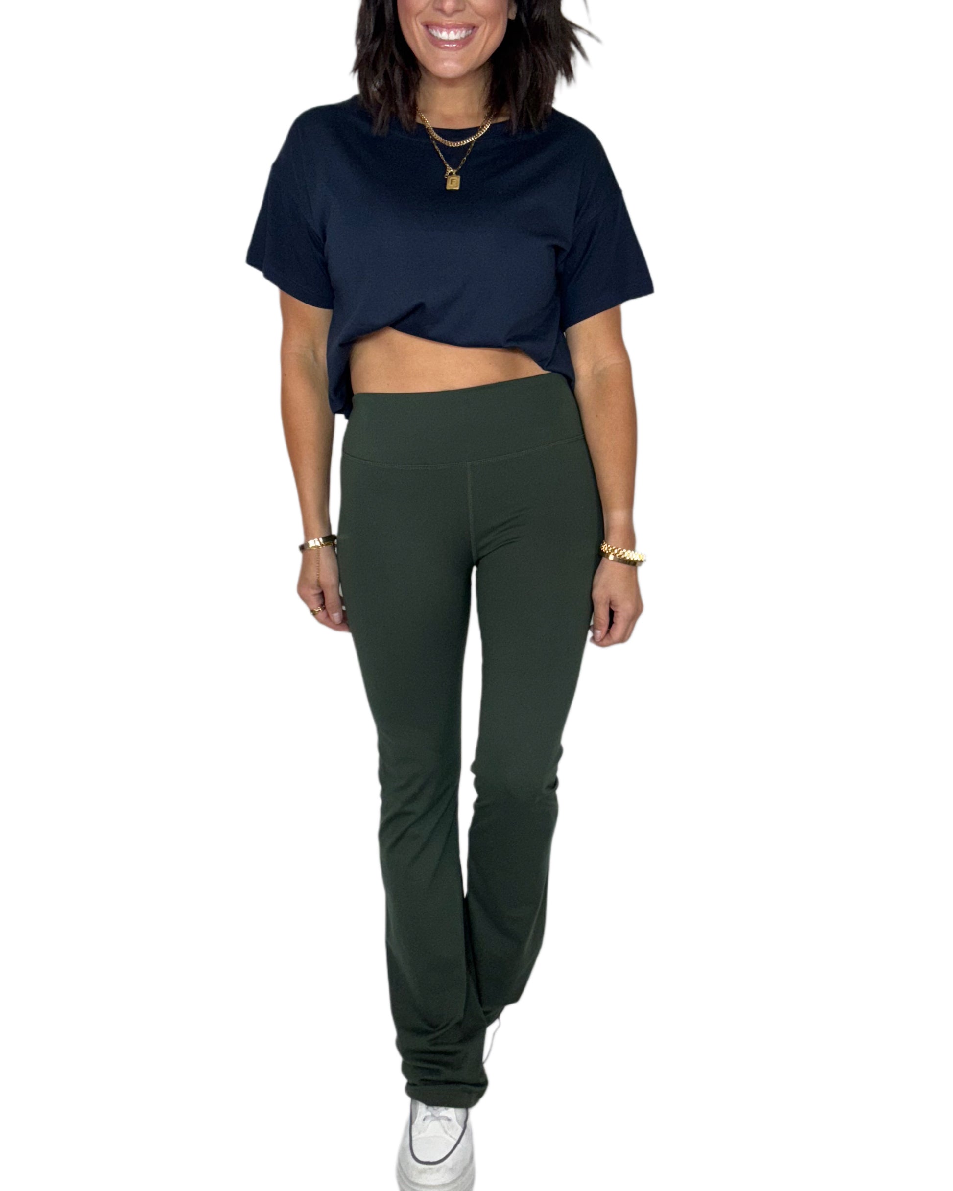 Woman wearing a navy top and forest green bootcut leggings on a white background