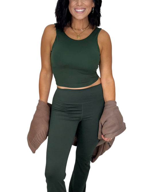 Woman wearing a green athletic outfit with brown knit sweater on a white background