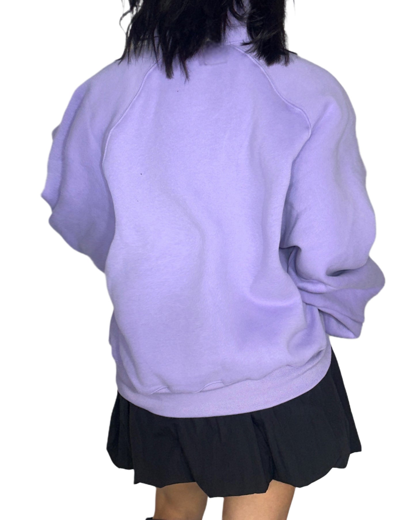 Back profile of a woman wearing a light purple sweatshirt and black skirt on a white background