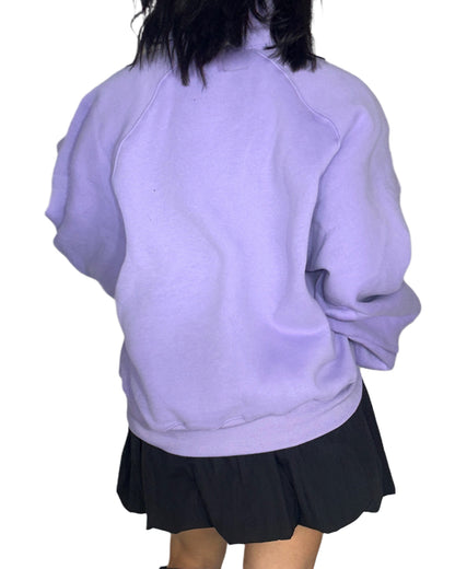 Back profile of a woman wearing a light purple sweatshirt and black skirt on a white background