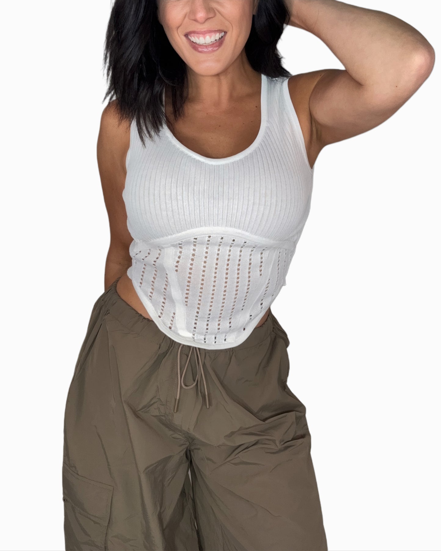 Woman wearing a white knit tank top with green pants and a white background 
