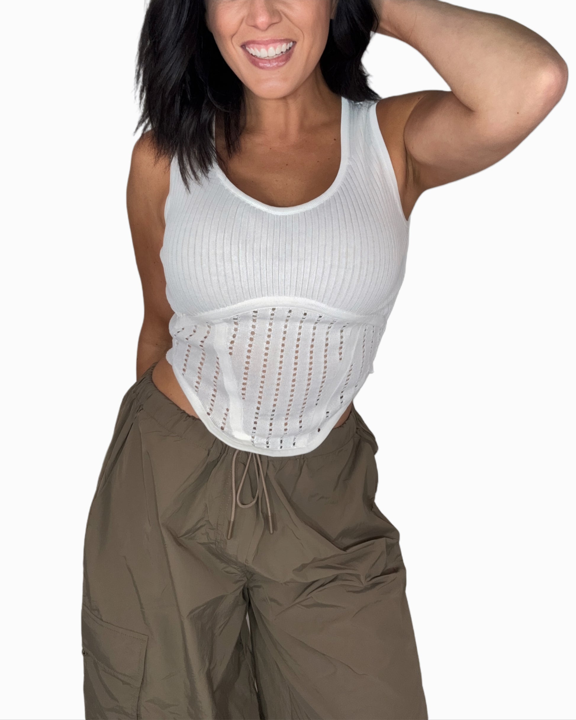 Woman wearing a white knit tank top with green pants and a white background 