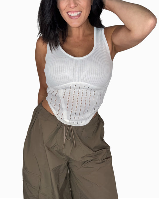 Woman wearing a white knit tank top with green pants and a white background 