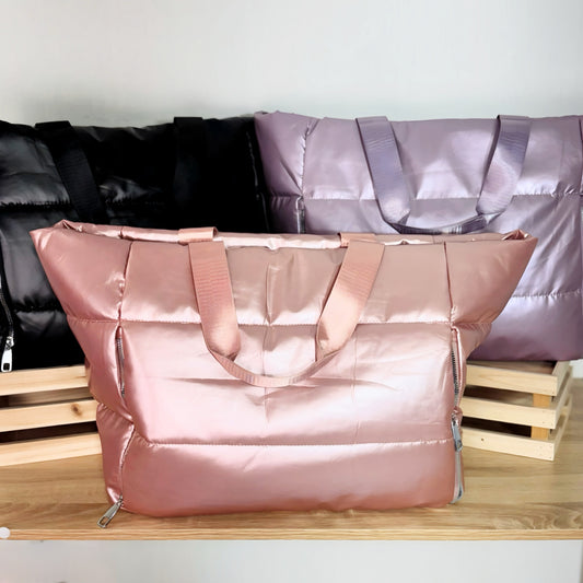 Large puffer tote bags in pink, black and lavender on a white background and light wood table 