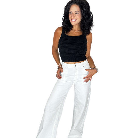 Woman wearing a knit black top with white pants on a white background