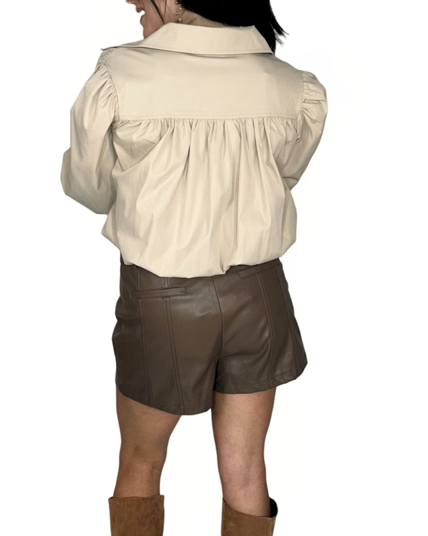 Person wearing a beige shirt and brown leather shorts on a white background