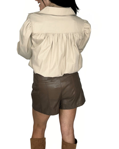 Person wearing a beige shirt and brown leather shorts on a white background
