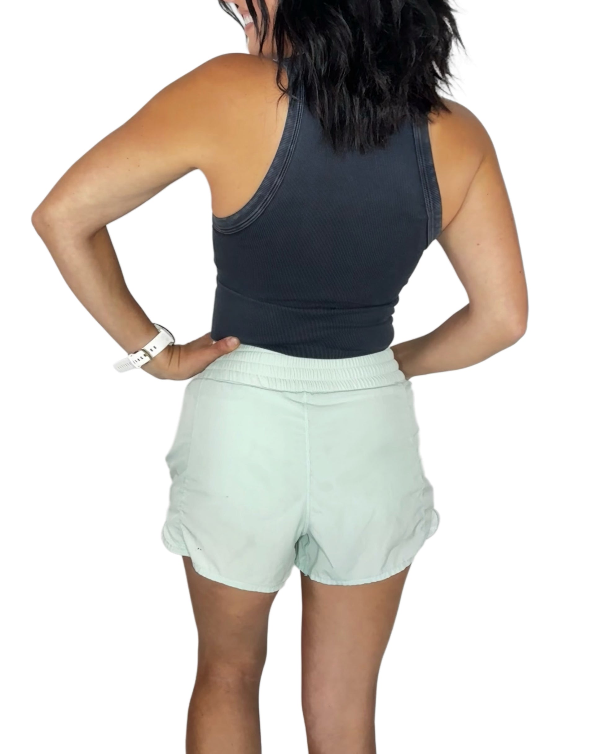 Back profile of a woman wearing a black ribbed vintage tank, with light green shorts on a white background