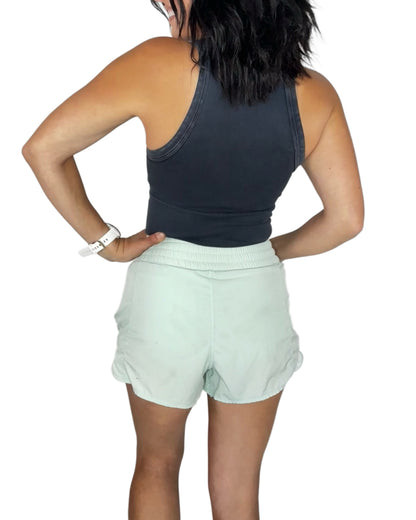 Back profile of a woman wearing a black ribbed vintage tank, with light green shorts on a white background