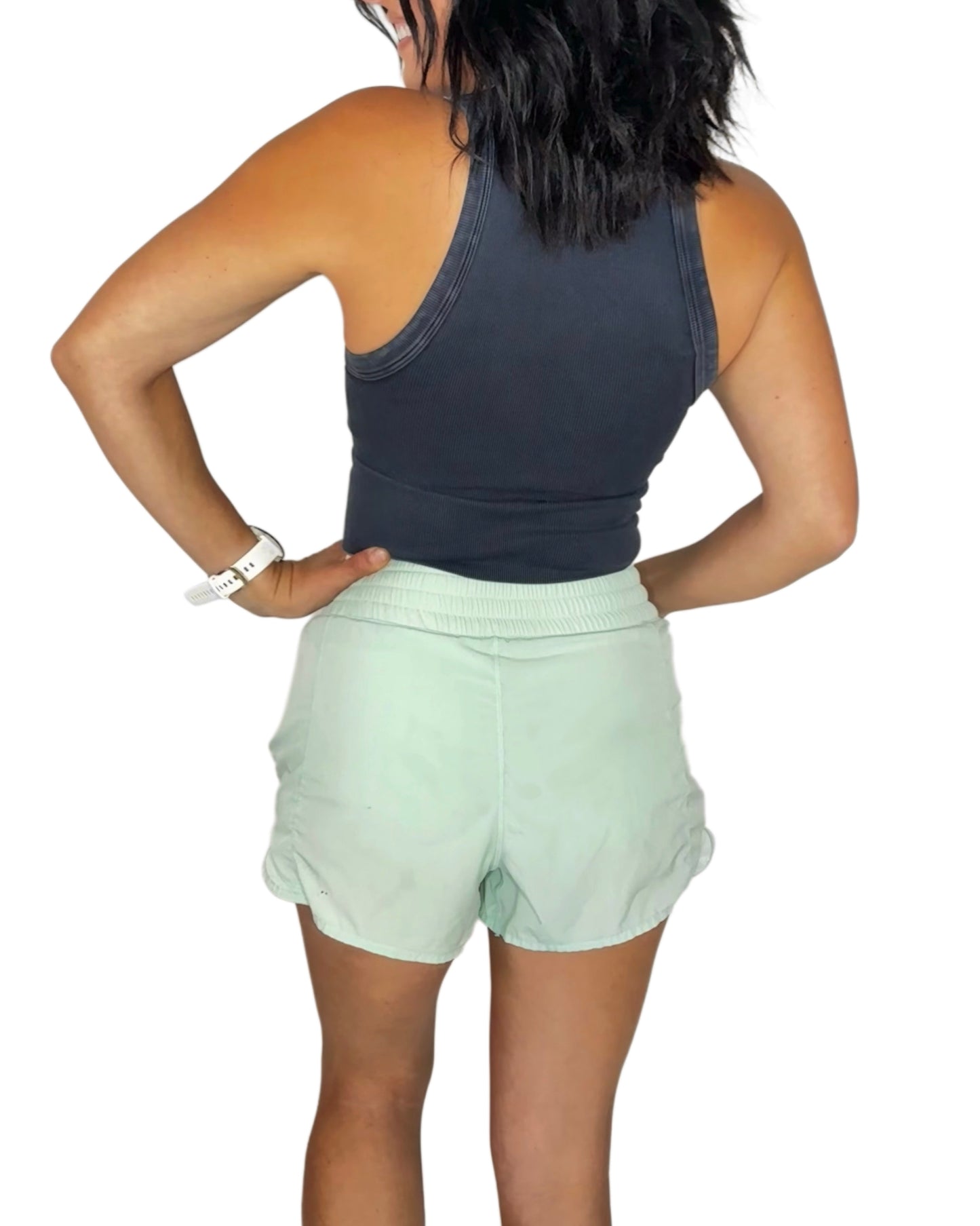 Back profile of a woman wearing pale green shorts with a black ribbed vintage tank on a white background