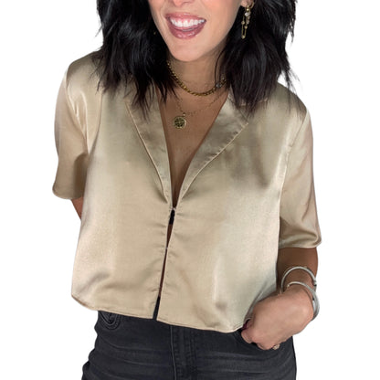 Close up of a woman wearing a gold satin blouse and dark jeans on a white background