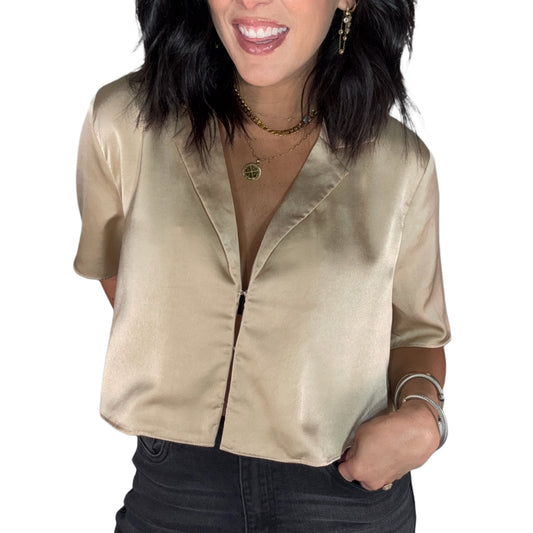 Close up of a woman wearing a gold satin blouse and dark jeans on a white background