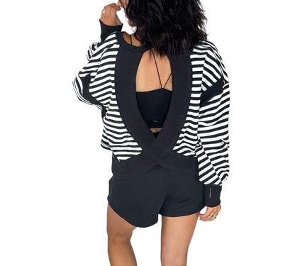 Back profile of a woman wearing black terry shorts with a striped black and white sweatshirt on a white background