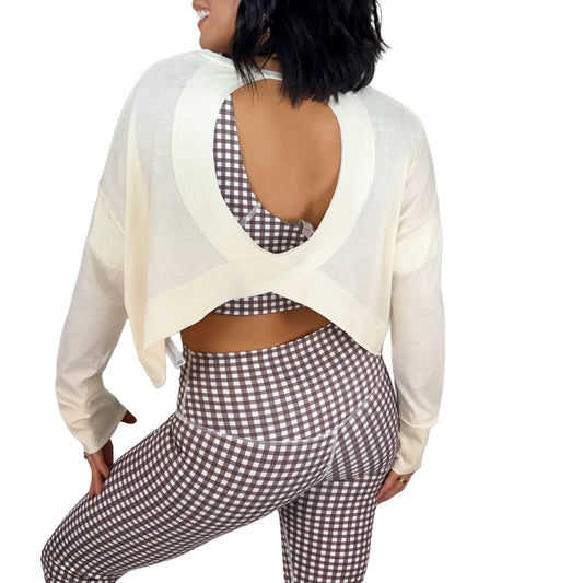Woman wearing a cream open-back top and brown checkered pants on a white background