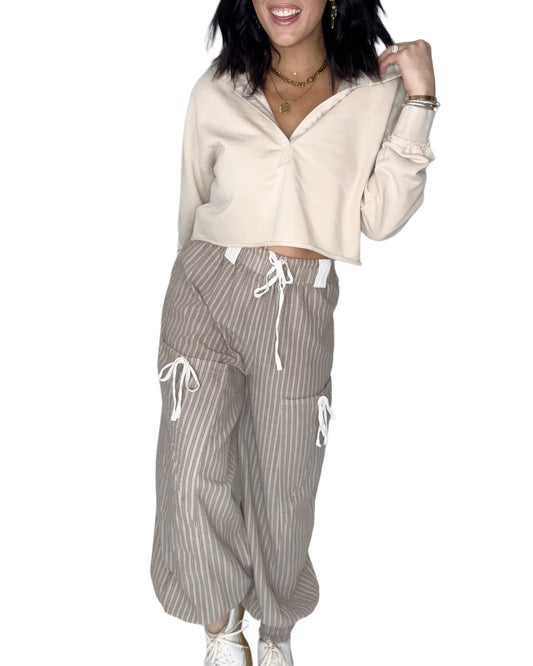 Woman wearing a beige cropped hoodie and striped pants on a white background